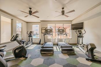A spacious gym with treadmills, elliptical machines, and a fan.